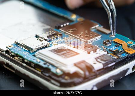 Technician repairing inside of mobile phone by soldering iron. Integrated Circuit. the concept of data, hardware, technology. Stock Photo