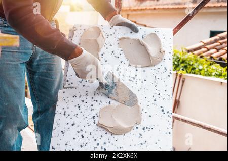Mason applies glue to a thermal cladding on a construction site Stock Photo