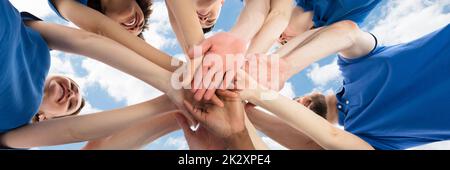 Happy Multiracial Janitors Stacking Hands Against Cloudy Sky Stock Photo