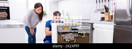 Serviceman Repairing Dishwasher In Kitchen Stock Photo