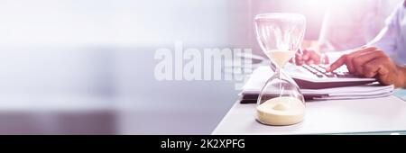 Hourglass In Front Of Businessperson Calculating Invoice Stock Photo