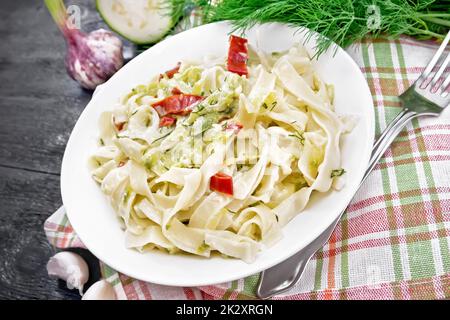 Fettuccine with zucchini and hot peppers in plate on black wooden board Stock Photo