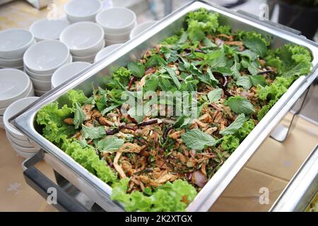 Larb Moo, sprinkled on top with mint leaves in buffet line. The container is a rectangular stainless steel tray with small white cups arranged on the side. Selective focus. Stock Photo