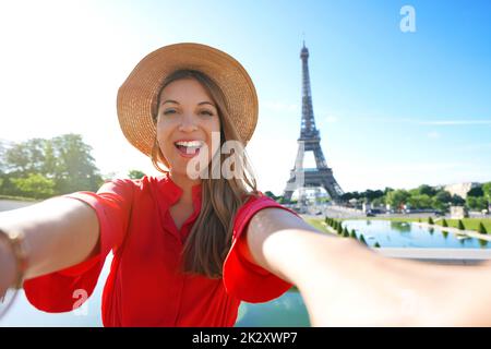 Excited fashion woman with red dress and hat has fun making self portrait with Eiffel Tower on the background in Paris, France. Stock Photo