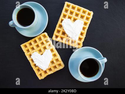 Delicious Belgian waffles with cream on a black background and two cups of coffee. Stock Photo