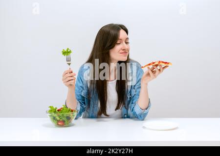 Young beautiful woman on a diet wants to choose pizza instead of salad Stock Photo