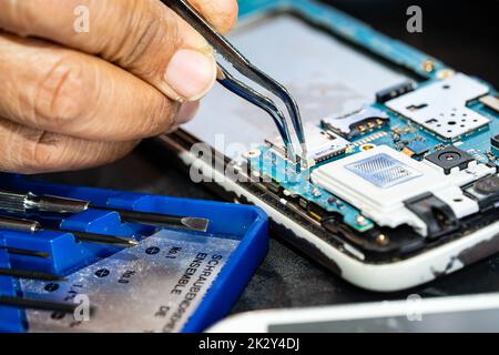 Technician repairing inside of mobile phone by soldering iron. Integrated Circuit. the concept of data, hardware, technology. Stock Photo