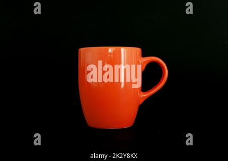 Profile view of orange color tea mug or cup isolated on dark background. Stock Photo