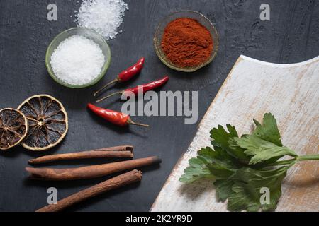 A top view shot of different kinds of food, including red chilies, dried lemons, seasonings, cinnamon, and celery on a hard black surface Stock Photo