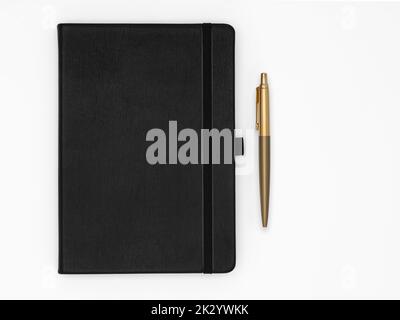 Black notebook closed and gold pen next to it on white background Stock Photo