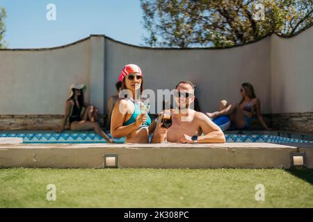 portrait of a latin couple leaning on the edge of a swimming pool Stock Photo