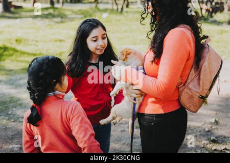Young woman with her two daughters on the grass and playing with a golden retriever puppy in the park Stock Photo