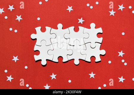 Jigsaw puzzle pieces in the middle of red background with snowflakes and stars. Christmas winter abstract festive background with space for Xmas Stock Photo
