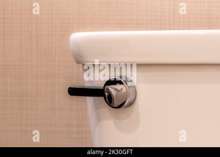 Close up image of a chrome toilet flush lever with a reflection of toilet paper. Stock Photo