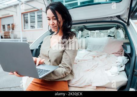 Woman using laptop in front of car trunk Stock Photo