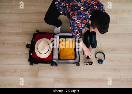 Mature man picking up camera by suitcase on floor at home Stock Photo