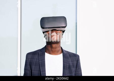 Smiling young man wearing VR glasses in front of wall Stock Photo