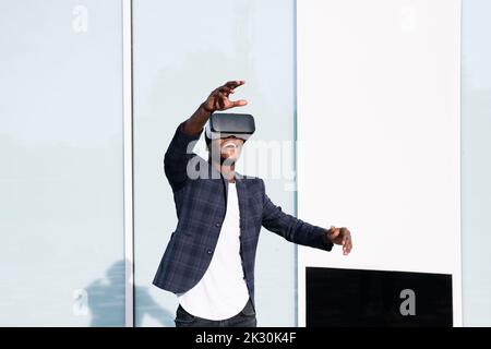 Smiling young man wearing VR glasses gesturing in front of wall Stock Photo