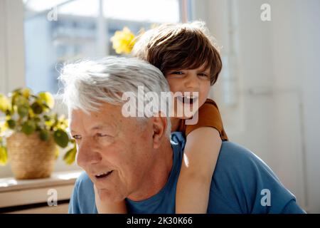 Happy senior man giving piggyback ride to grandson at home Stock Photo