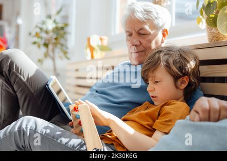 Grandfather looking at grandson with abacus sitting on sofa Stock Photo