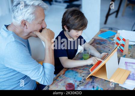 Smiling boy using tablet PC by grandfather at home Stock Photo