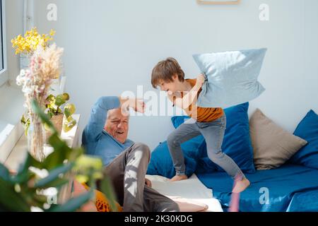 Happy boy playing pillow fight with grandfather on sofa at home Stock Photo