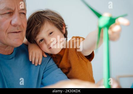 Smiling cute boy looking at wind turbine model with grandfather at home Stock Photo