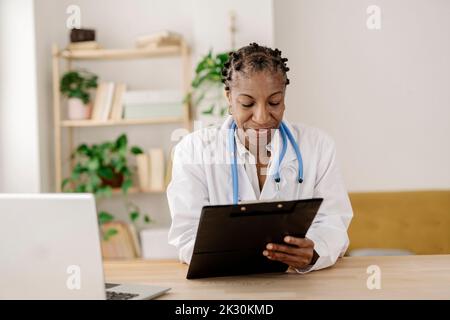 Smiling doctor with clipboard working at home office Stock Photo