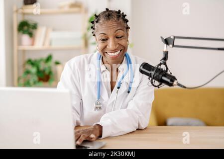 Smiling female doctor with microphone using laptop at home office Stock Photo