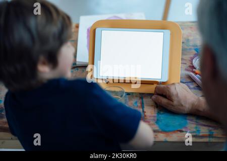 Boy using tablet PC with grandfather at home Stock Photo