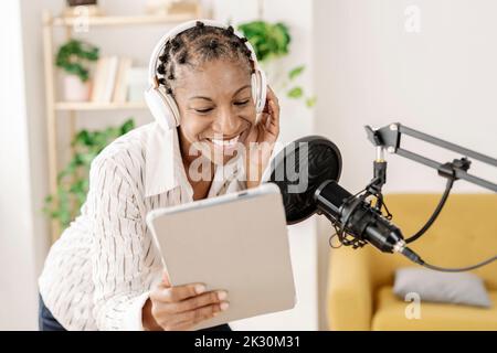 Smiling freelancer using tablet PC and recording podcast through microphone at home office Stock Photo