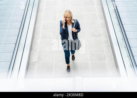 Businesswoman talking over phone walking on walkway Stock Photo