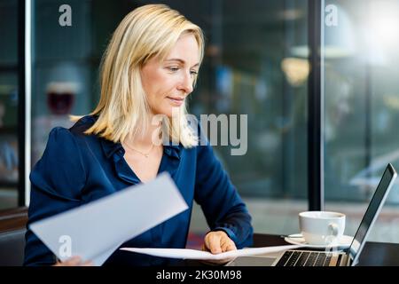 Smiling businesswoman with documents looking at laptop Stock Photo