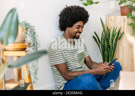 Happy man with Afro hairstyle using smart phone at home Stock Photo