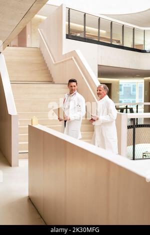 Doctors walking in corridor by railing at hospital Stock Photo