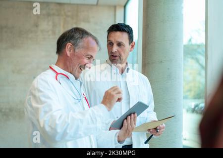 Doctor looking at happy colleague using tablet PC at hospital Stock Photo