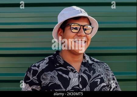 Happy young man with sunglasses and hat in front of wall Stock Photo
