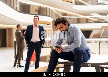 Businessman using mobile phone with colleagues in background at office Stock Photo