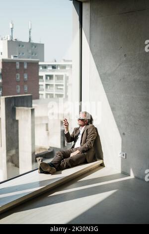Senior businessman with VR glasses looking through window at office Stock Photo