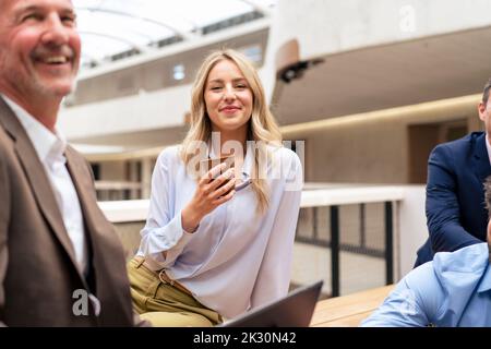 Smiling businesswoman having coffee by colleagues at office Stock Photo