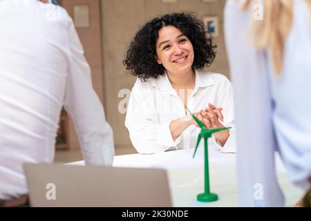 Smiling businesswoman discussing over wind turbine model with colleagues Stock Photo