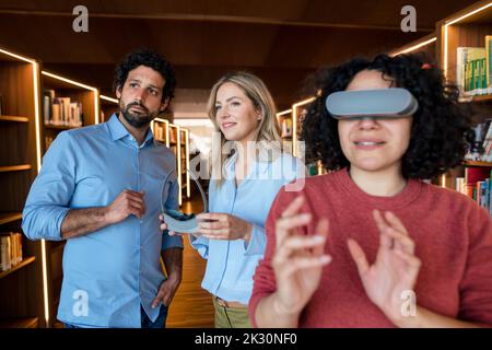 Multiracial colleagues with VR glasses in illuminated library Stock Photo