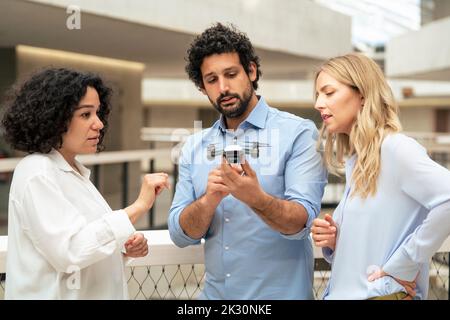 Multiracial colleagues discussing over drone in office corridor Stock Photo