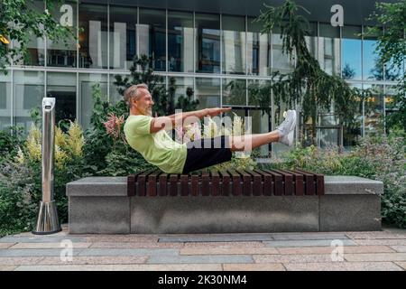 Mature man practicing boat position yoga on bench Stock Photo