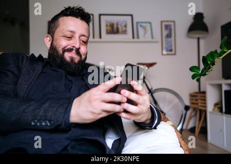 Smiling businessman text messaging through smart phone at home Stock Photo