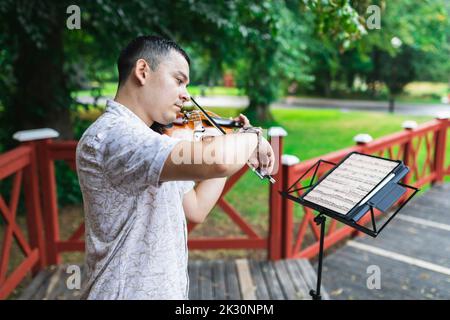 Violinist playing violin looking at sheet music in park Stock Photo