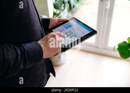 Hand of man adjusting room temperature through tablet PC at home Stock Photo