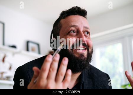 Smiling businessman talking on headset gesturing at home Stock Photo