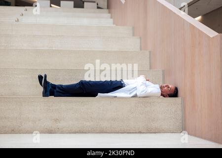Overworked mature doctor lying on step in hospital Stock Photo