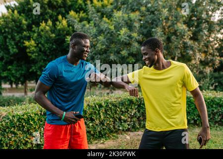 Happy young men greeting each other with elbow bump at park Stock Photo